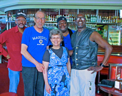 Photo shows Dona and Gene standing in front of a bar with 3 smiling black men, two of whom have their hands on their hips.